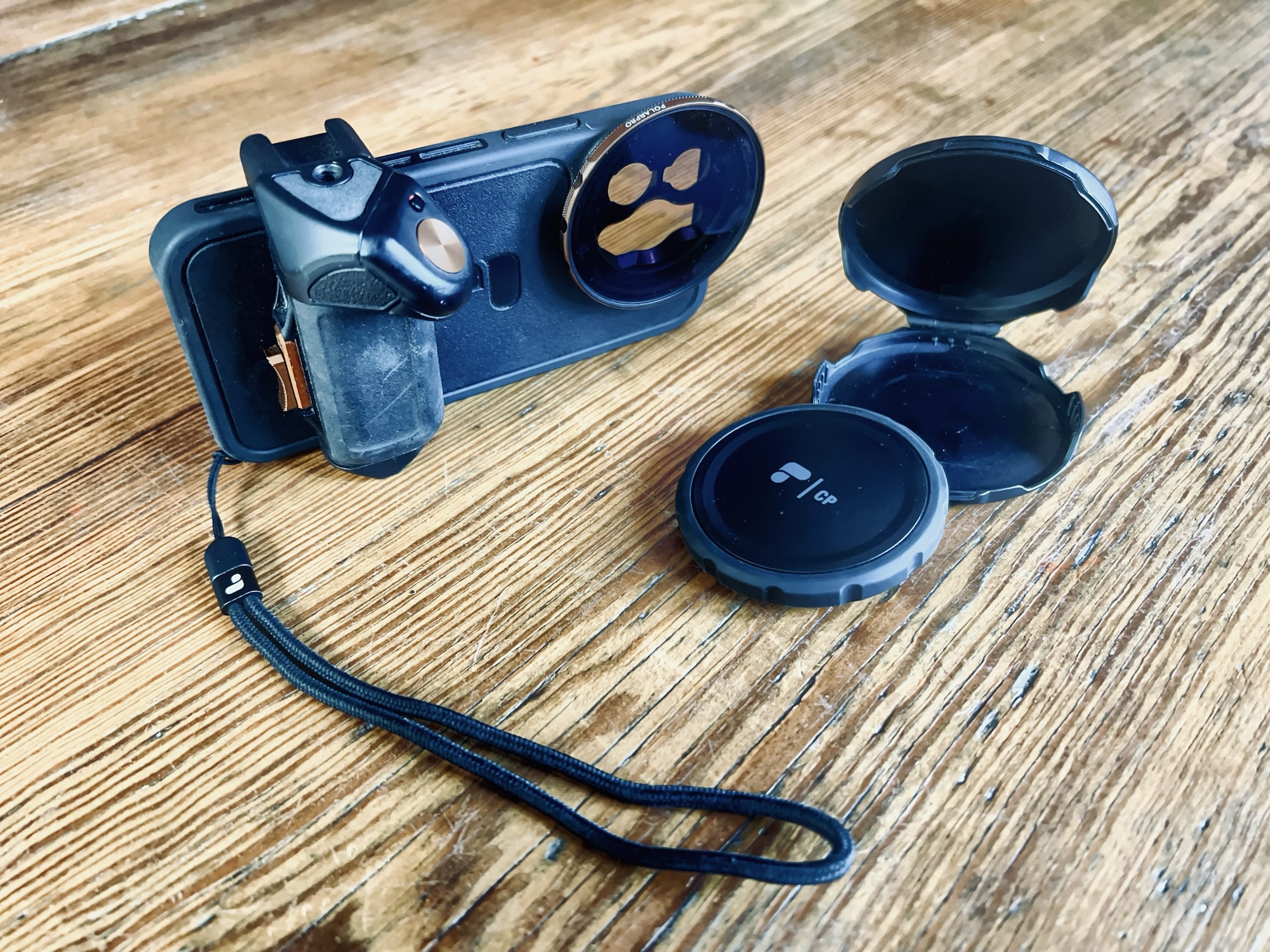 Eine Handyhülle vom Typ PolarPro LiteChaserPro für ein iPhone 13 Pro, mit Griff (montiert), Bluetooth Shutter, aufgeschraubtem Polfilter und Deckel und Hülle für den Filter.