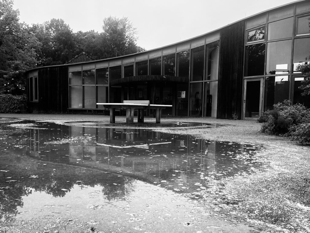 Platz vor dem Haus für Spiel und Bewegung mit Reflektionen in den Pfützen davor. Schwarz-weiß.