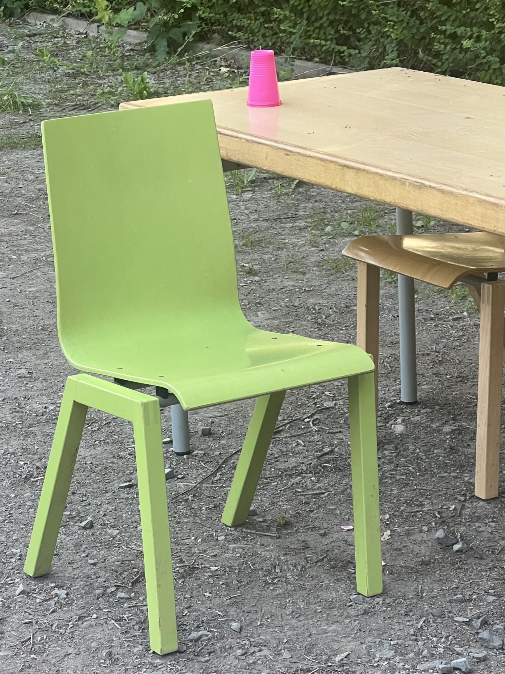 Reste des Getränkestandes von der Johanni-Feier: Schultisch mit grünem Stuhl auf dem großen Parkplatz. Ein pinker Becher steht auf dem Tisch.