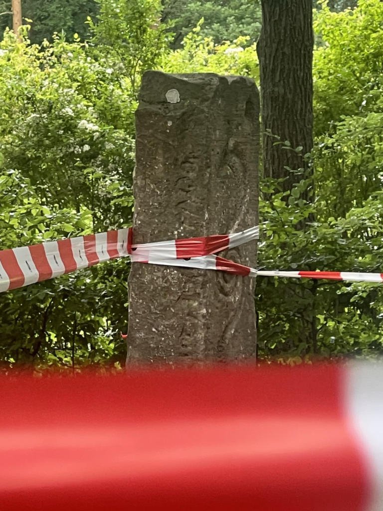 Absperrband um Steele und Bäume, grüne Blätter im Hintergrund