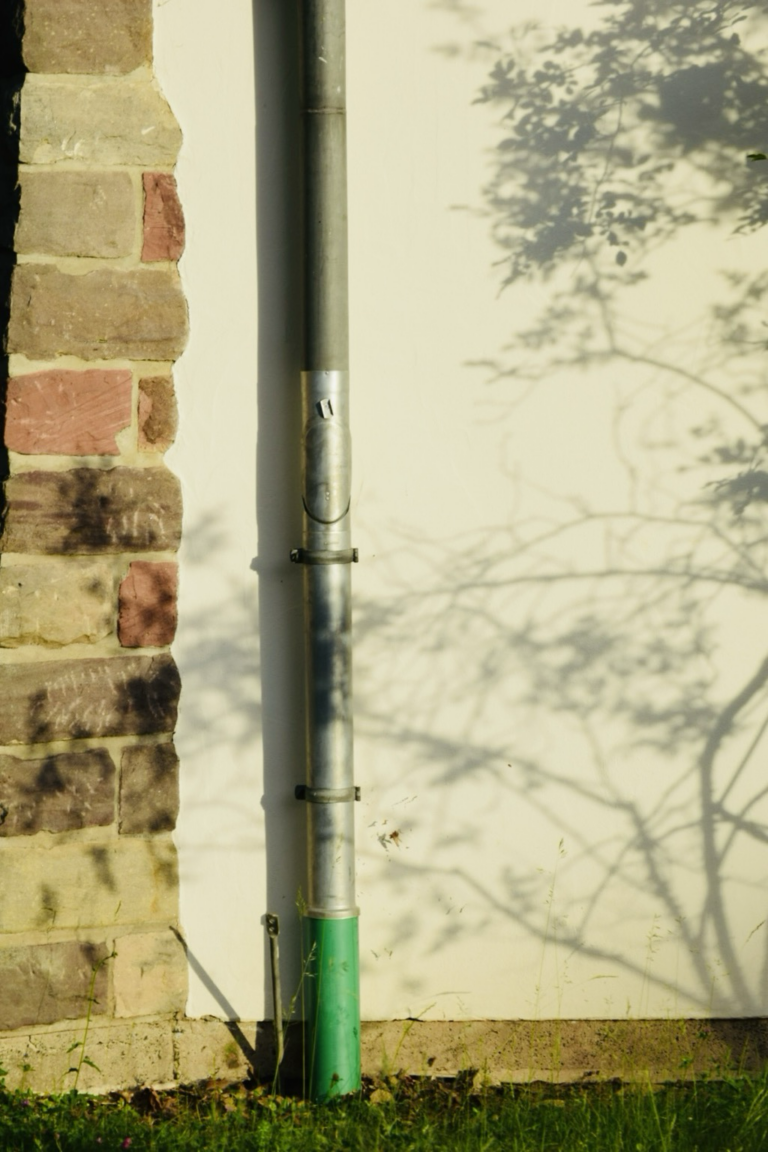 Hauswand mit Regenrohr und Schatten eines Busches